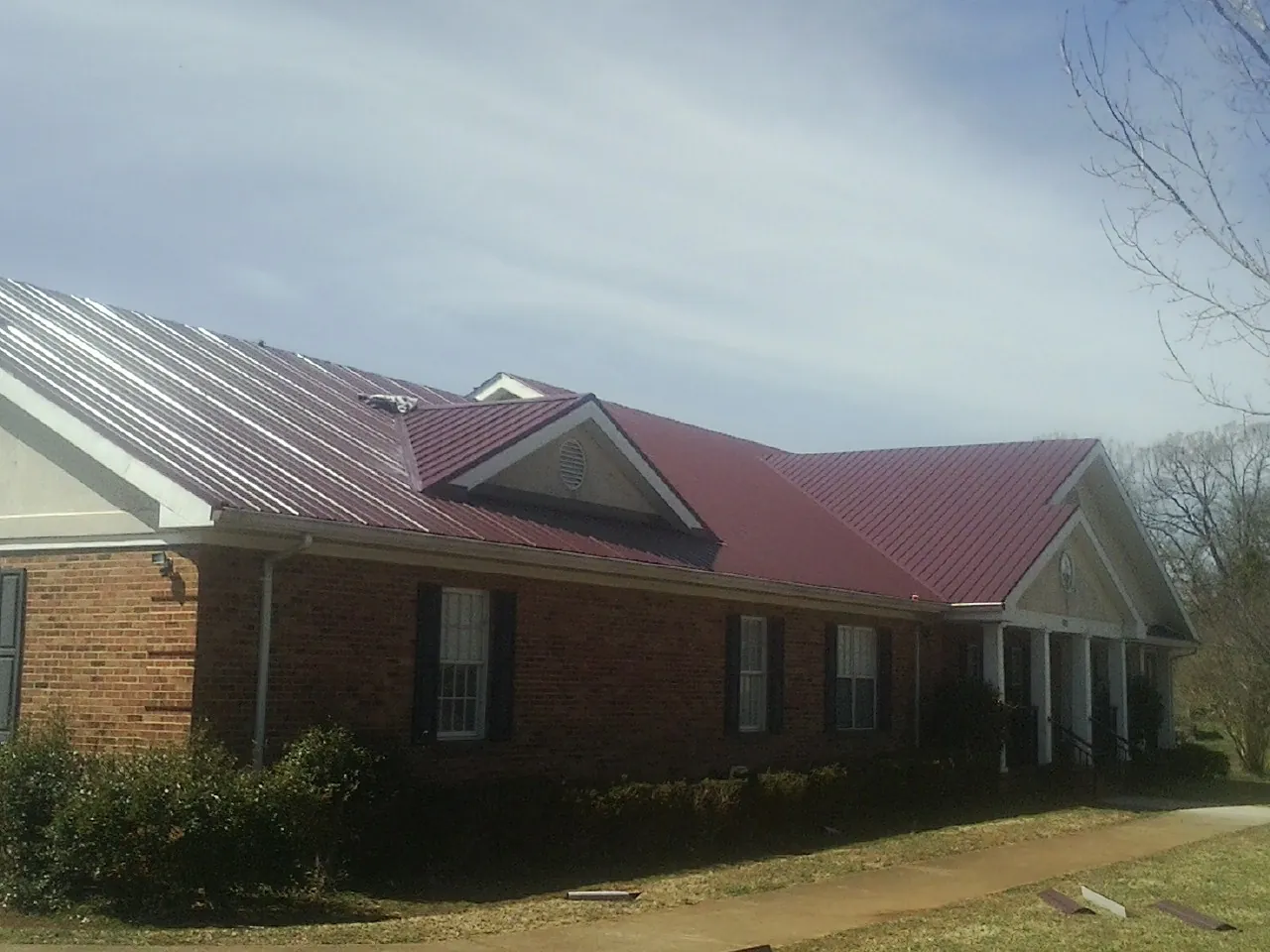 Red metal roof with gabled entries on a long brick building, from a Hail Damage Roof Repair job in Dryden