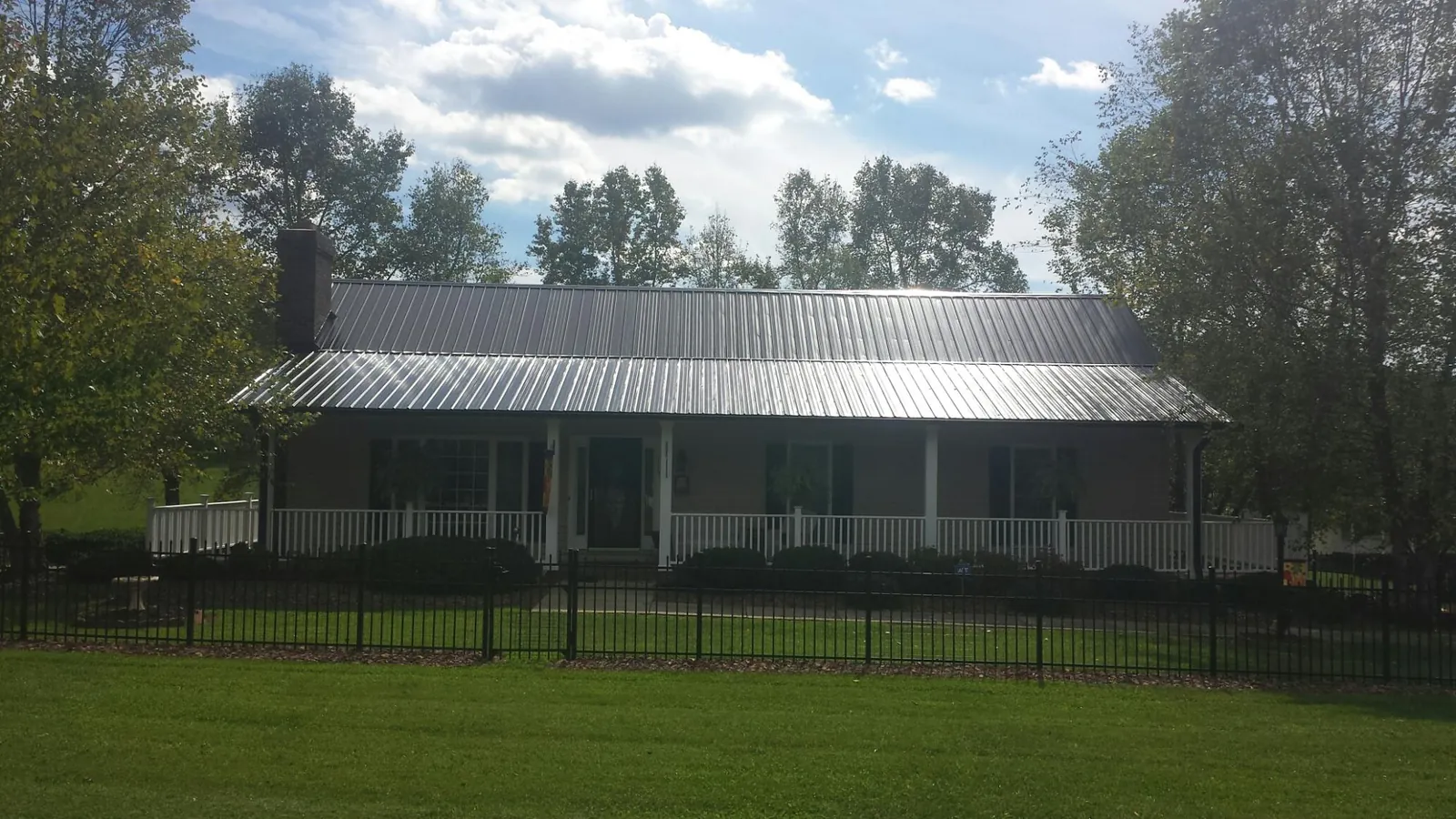 Gray metal roof on a brick ranch with a full width front porch — Gutter Guard Installation work by our crew in Dryden